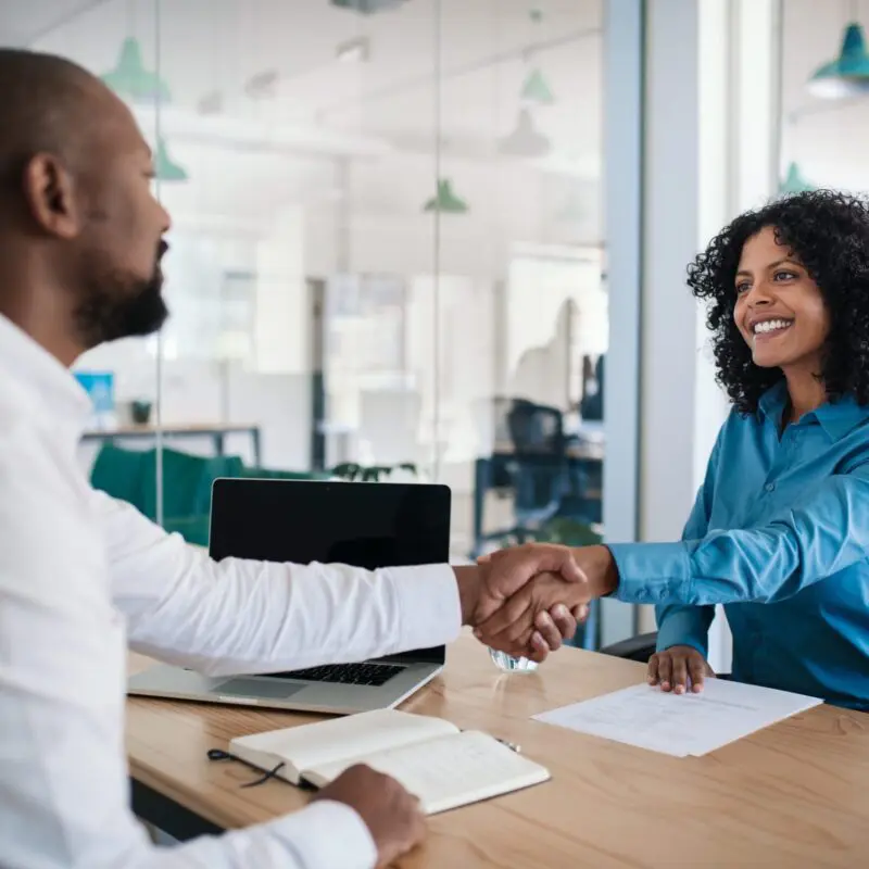 two diverse people shaking hands across a desk